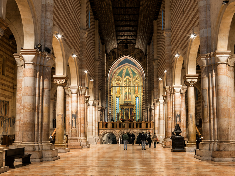 Interno di una cattedrale storica con ampie arcate in pietra, colonne monumentali e pavimento geometrico, illuminato da una calda luce dorata.
