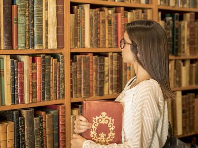 ragazza con libro sotto braccia guarda scaffale di libri antichi all'interno di una biblioteca