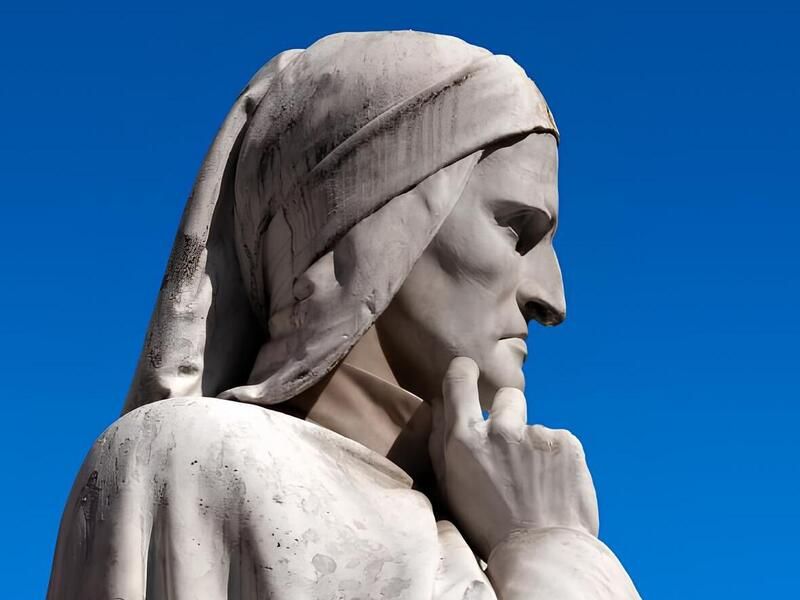 Statua di Dante Alighieri in marmo bianco su sfondo di cielo azzurro, ripresa di profilo con la mano al mento in posa meditativa