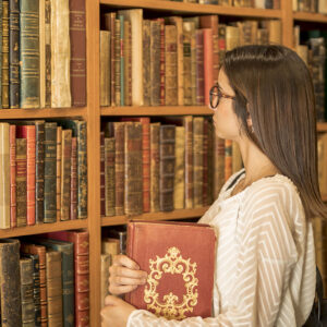 ragazza con libro sotto braccia guarda scaffale di libri antichi all'interno di una biblioteca