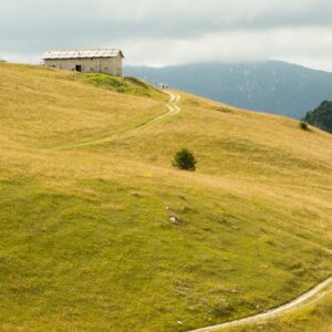 Rifugio in pietra sull’altopiano della Lessinia, circondato da prati dorati e raggiunto da un sentiero sterrato, con montagne sullo sfondo